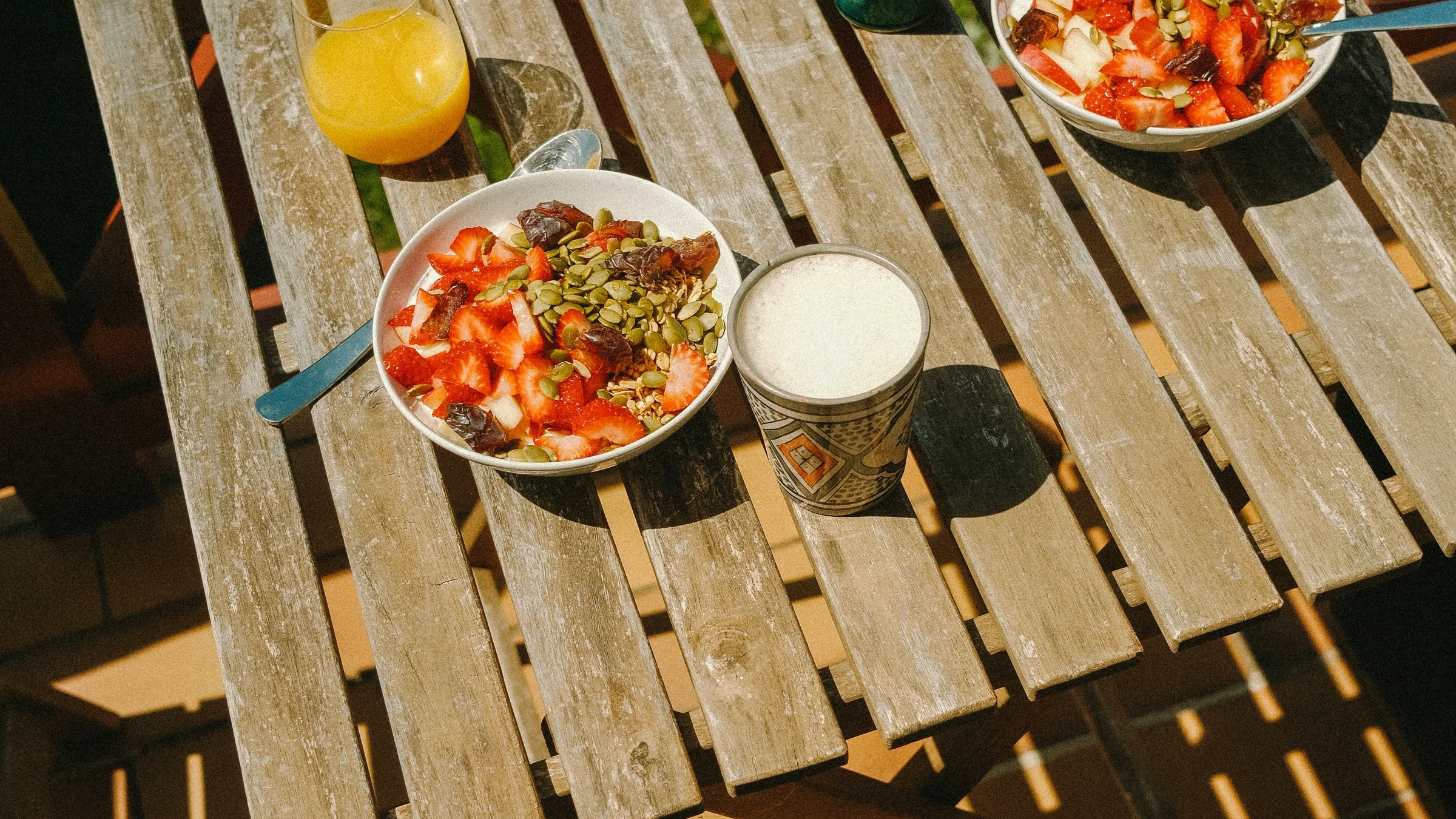 Breakfast bowls and drinks on an outdoor table, with a cup beside the meal