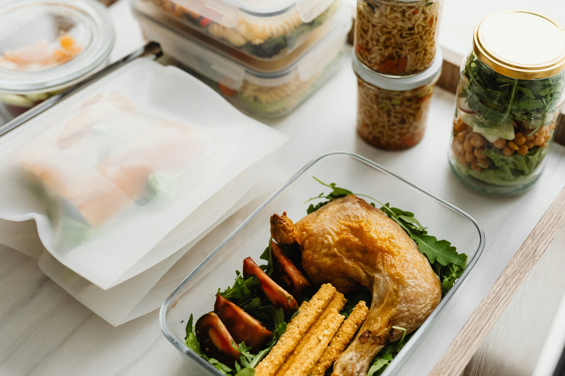 Meal-prep containers with roast chicken, grains, and vegetables on a kitchen counter