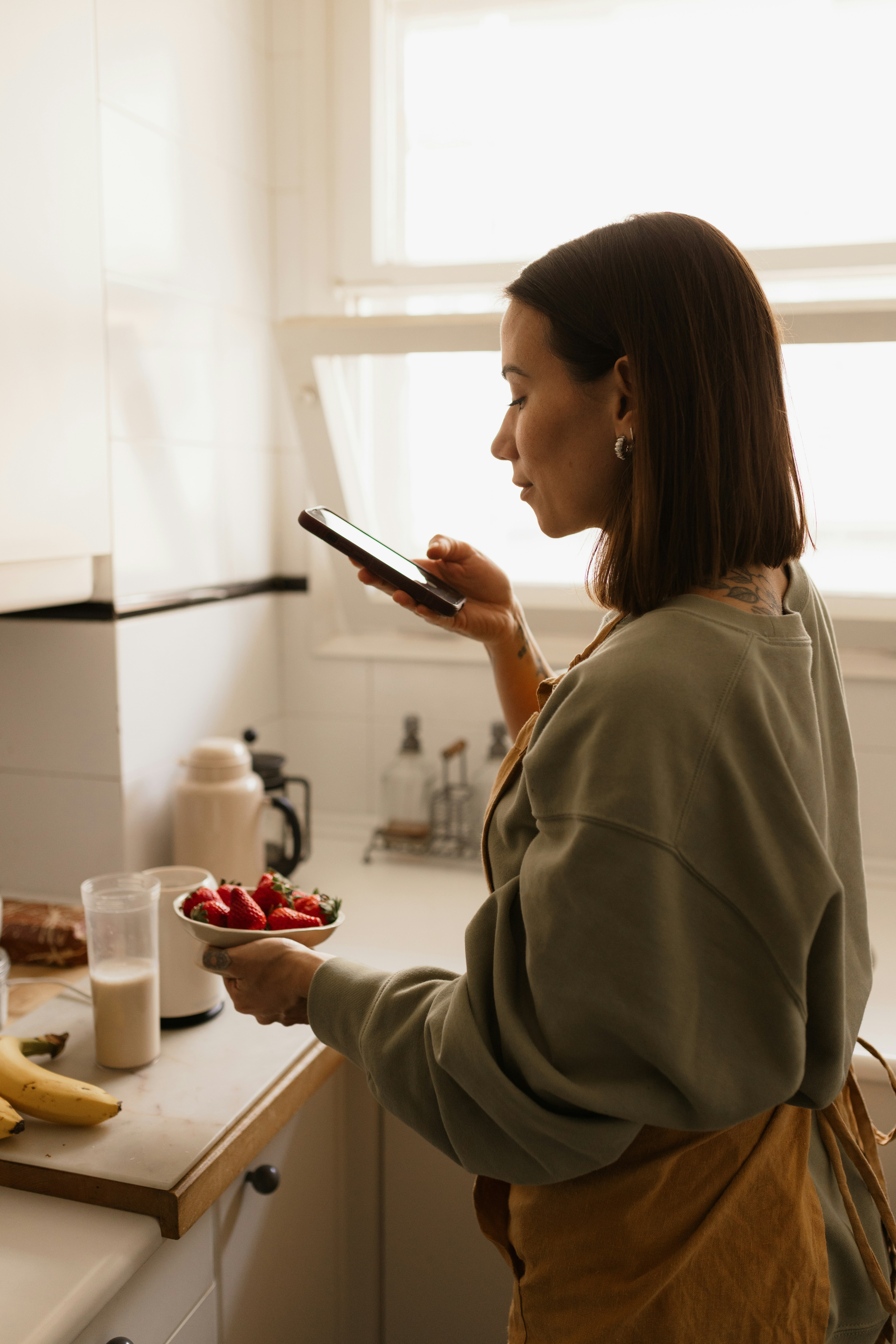 Person checking a phone while preparing breakfast, representing a calm symptom and treatment-context log